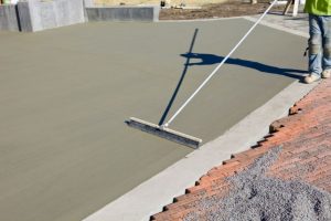 Concreter using a broom finish tool on a freshly poured residential concrete slab
