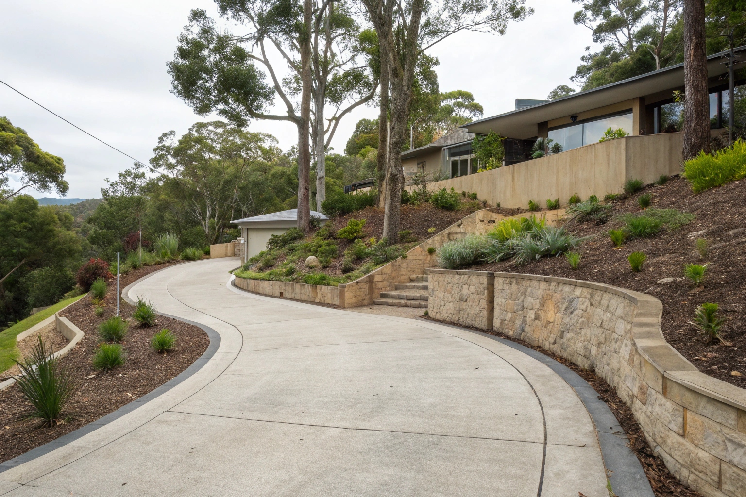 Curved plain concrete driveway on a sloped residential property