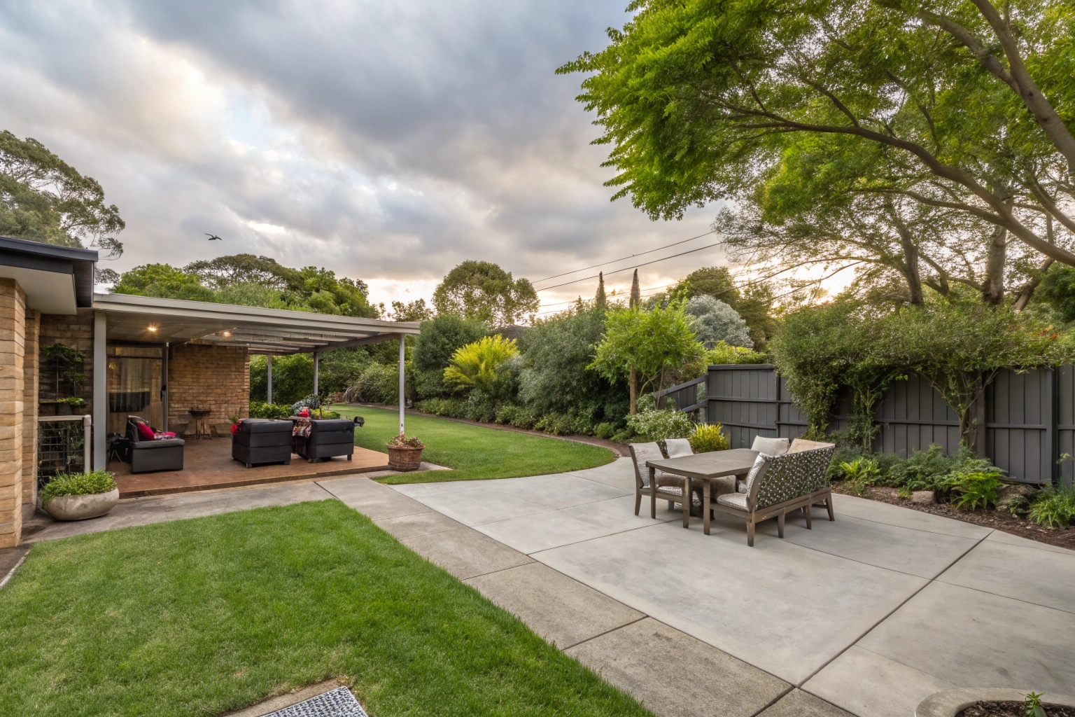 Concrete patio in a Macgregor backyard with outdoor furniture and shade trees